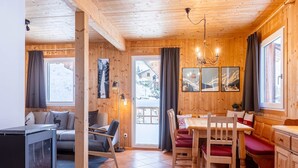 A cozy wooden cabin with a fireplace, a dining area, and a seating area with a view of the snowy landscape.