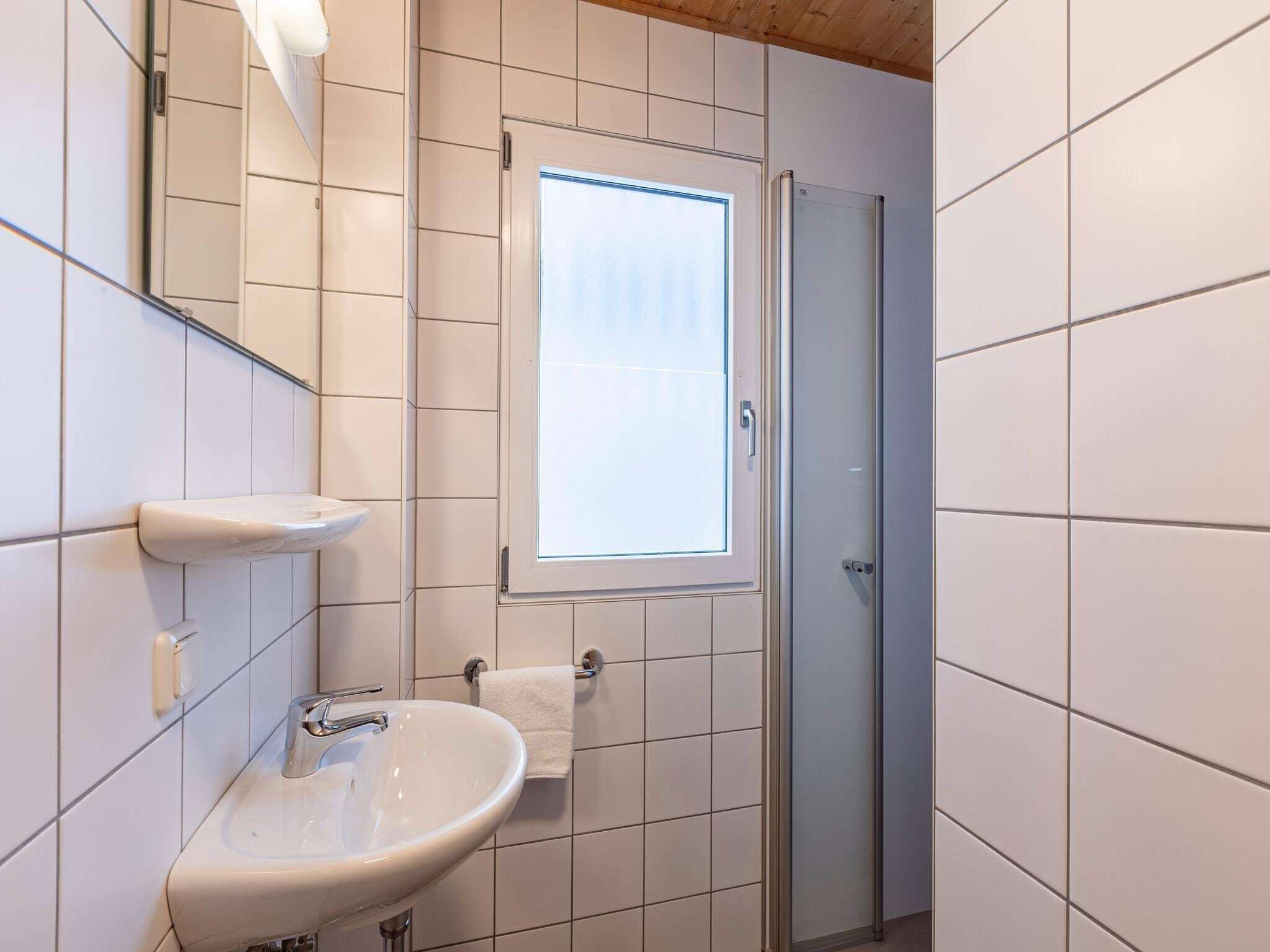 Une salle de bain avec un lavabo blanc, un miroir, un porte-serviettes et une fenêtre.