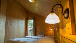 A wooden cabin room with a bed, a window, and a wall-mounted light fixture.