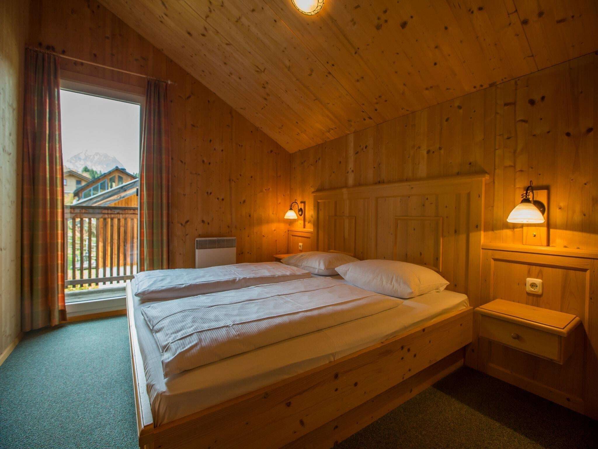 Une chambre dans une cabane en bois, avec un lit, deux tables de chevet et une fenêtre avec des rideaux.