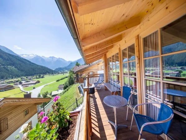A wooden balcony with a table and chairs, overlooking a mountainous landscape.