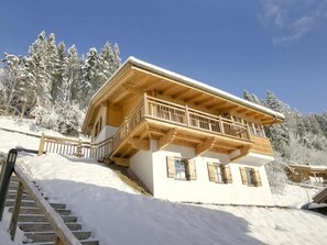Una cabaña de madera de dos pisos con un balcón, rodeada de árboles cubiertos de nieve.