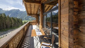 A wooden deck with a table and chairs overlooking a mountainous landscape.