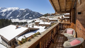 A wooden balcony with a view of snow-covered mountains, wicker chairs, and a rustic interior.