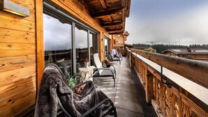 A wooden balcony with a view of the landscape, a table with chairs, and a person sitting on a bench.