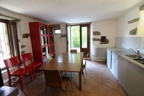 A dining area with a wooden table and red chairs, a kitchen with a sink and stove, and a window with a view of greenery.