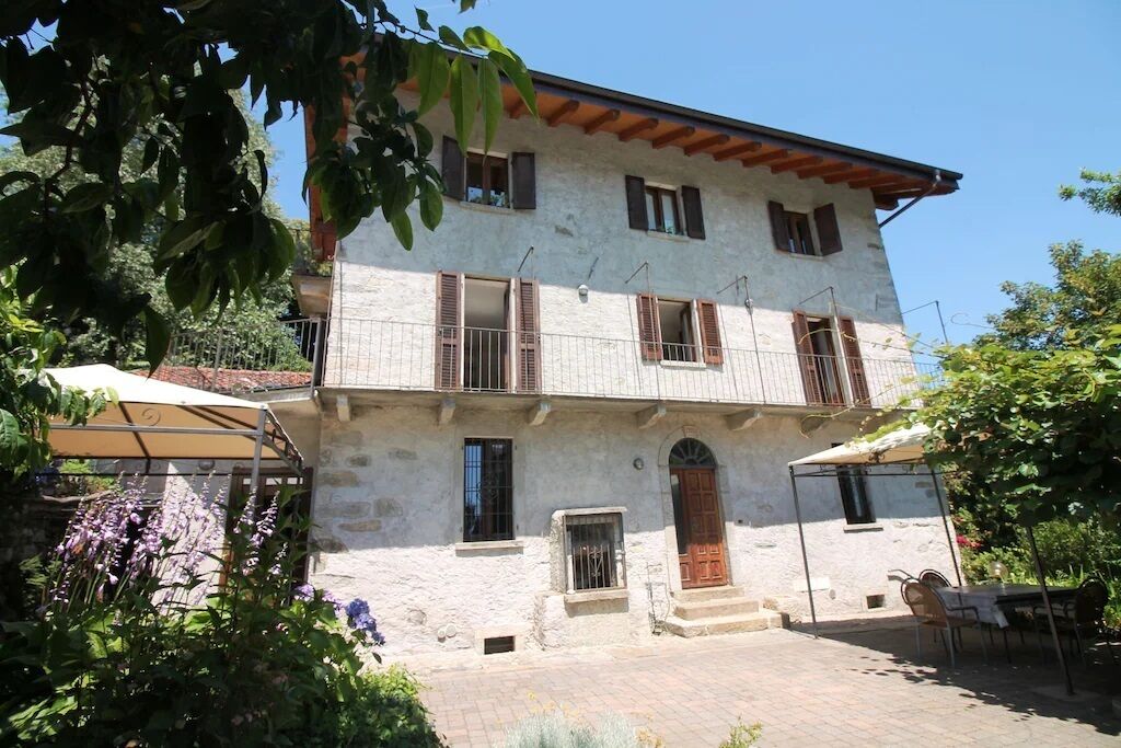A two-story stone building with a balcony, a wooden door, and a covered outdoor seating area.