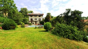 Ein zweistöckiges Haus mit Swimmingpool, umgeben von üppiger Vegetation und Bäumen.