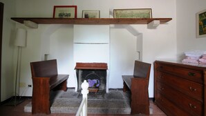 Ein Zimmer mit Kamin, hölzernen Bänken, einem Schmuckkästchen und einem Regal mit gerahmten Bildern.