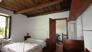 Ein Schlafzimmer mit Holzboden, einem Bett mit weißem Kopfteil, einem Nachttisch, einer Holzbank und einer Tür, die auf einen Balkon führt.