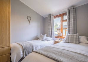 Quarto com duas camas, um guarda-roupa de madeira, uma decoração em formato de coração e uma janela com cortinas.