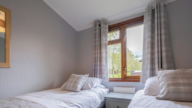 A bedroom with two beds, a window with curtains, a radiator, and a bedside table.