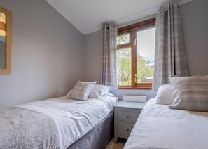 Quarto com duas camas, uma janela com cortinas, um radiador e uma mesa de cabeceira.