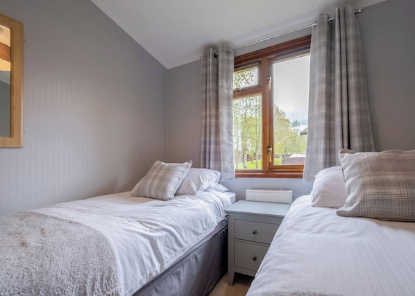 A bedroom with two beds, a window with curtains, a radiator, and a bedside table.