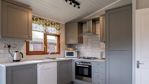 A modern kitchen with grey cabinets, a dishwasher, a microwave, a stove, and a window with a leaf-patterned curtain.