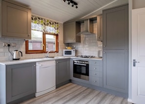 Cozinha moderna com armários cinza, lava-louças, micro-ondas, fogão e janela com cortina estampada com folhas.