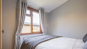 A bedroom with a bed, a window with curtains, a door, and a light fixture.
