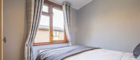 Une chambre à coucher avec un lit, une fenêtre avec des rideaux, une porte et un luminaire.