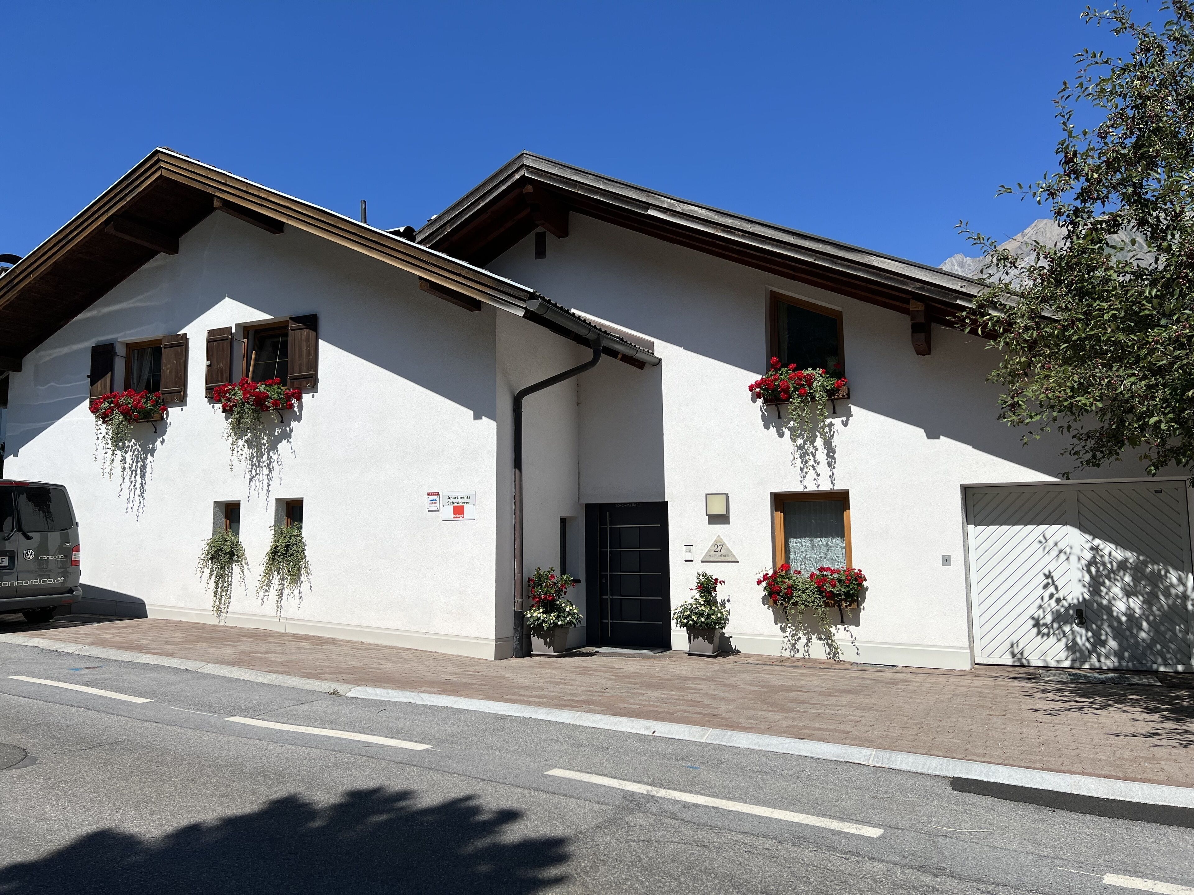Un immeuble de deux étages avec une façade blanche, de nombreuses fenêtres dotées de volets en bois et des jardinières au dernier étage.