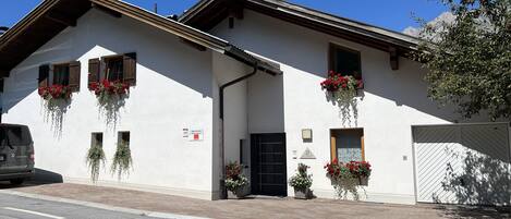 Un immeuble de deux étages avec une façade blanche, de nombreuses fenêtres dotées de volets en bois et des jardinières au dernier étage.