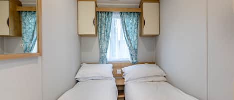 A small, narrow room with two beds, a mirror, and a window with curtains.