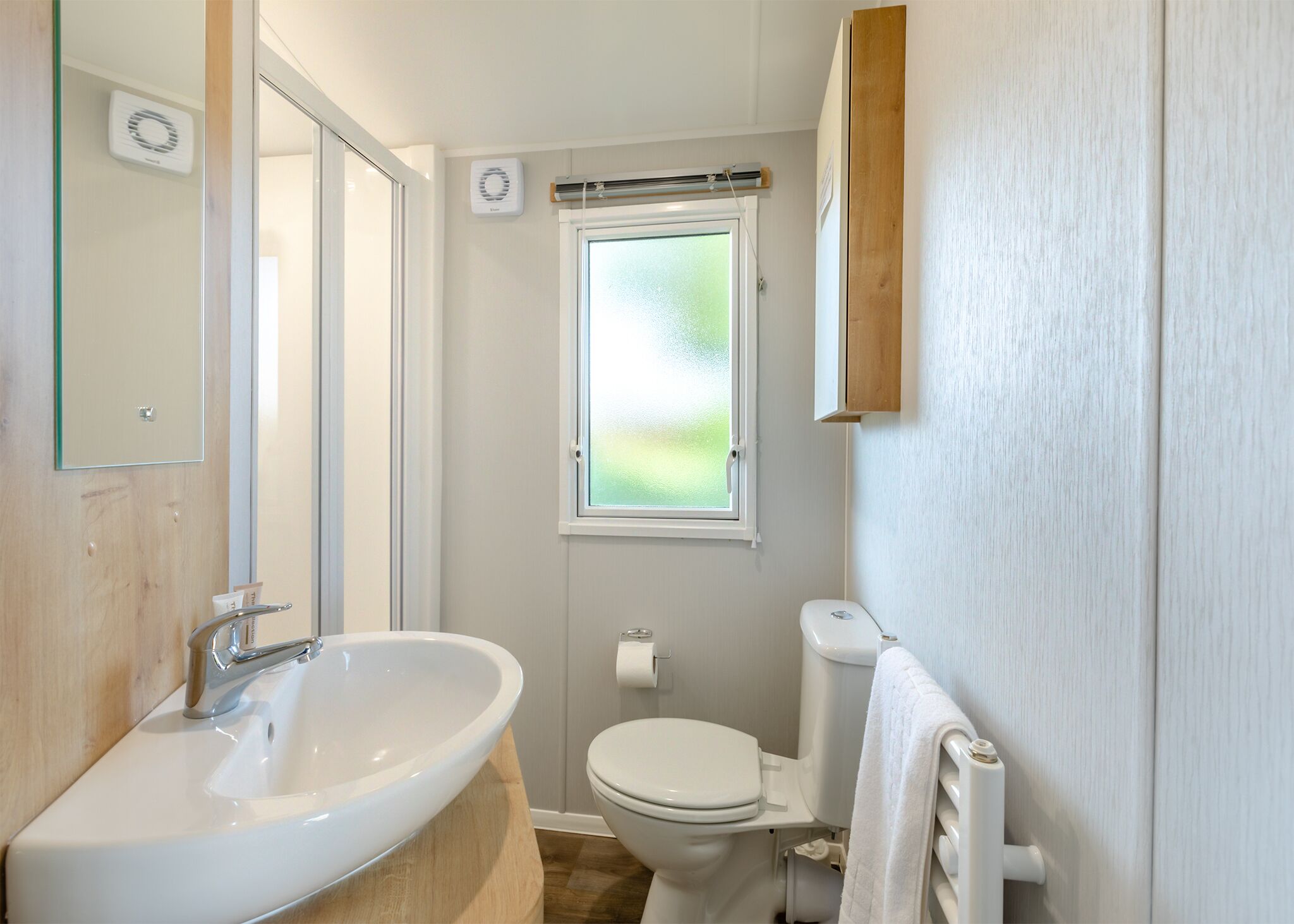 A bathroom with a white sink, toilet, and window.