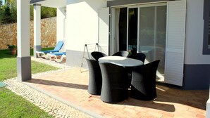 An outdoor patio with a table and chairs, a covered seating area, and a sliding glass door leading to a balcony. - Stevens Brown Apartment, Quinta do Lago, Algarve (nº95 R/C,)