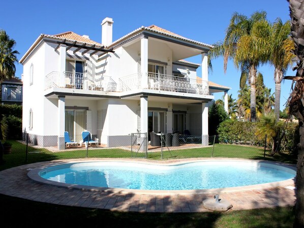 A two-story house with a swimming pool, a covered patio, and a fenced backyard.