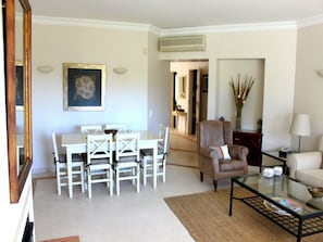 Un salon comprenant une table à manger, des chaises, un canapé, une table basse en verre et un vase décoratif.
