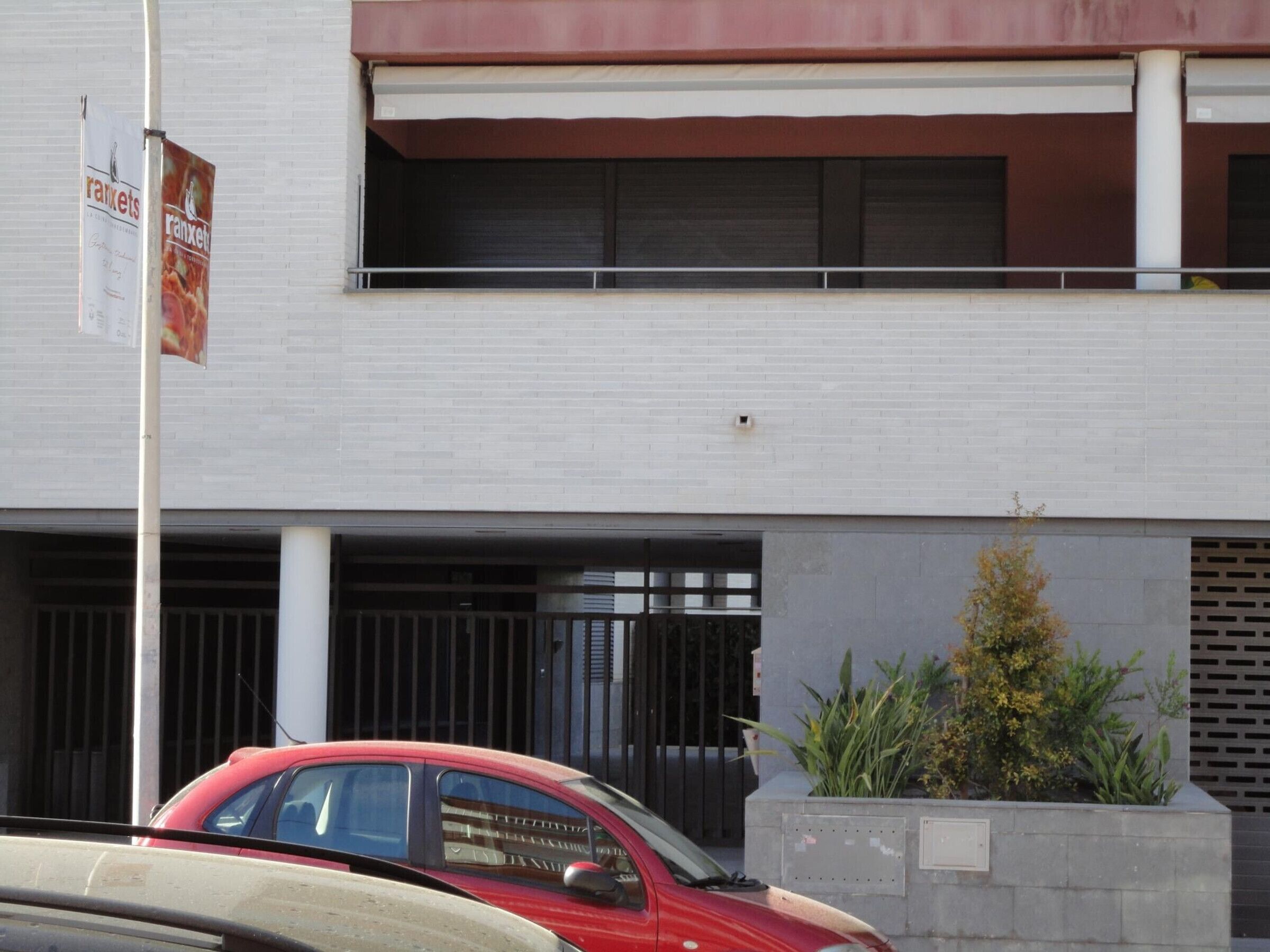 A building with a garage door, a red car parked in front, and a sign on the pole.