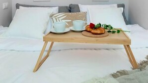 A neatly made bed with white linens, a wooden tray with cups and a croissant, and two wall-mounted light fixtures.