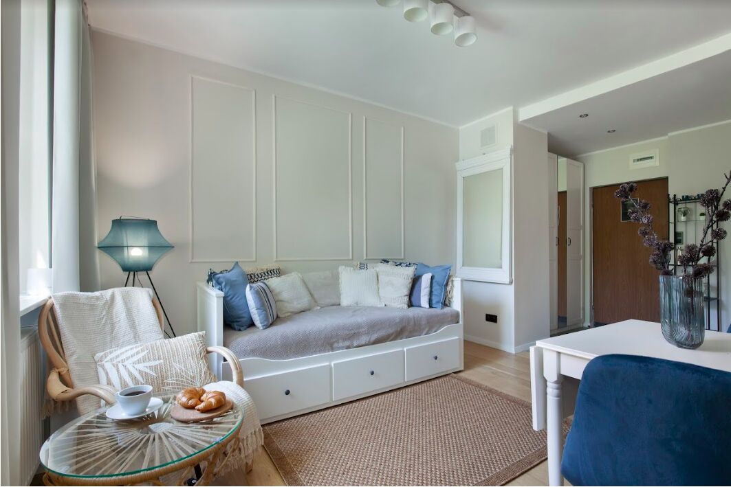 Une chambre avec un lit, une chaise, une table sur laquelle se trouvent une tasse et des pâtisseries, et une lampe.