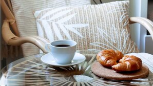 A glass table with a cup of coffee and a croissant on a saucer.