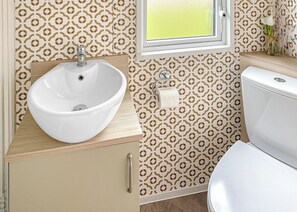 Un baño con lavamanos blanco, inodoro y papel tapiz estampado.