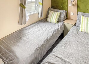 Una cama individual con una colcha a rayas y almohadas, una mesita de noche, una lámpara y una ventana con cortinas.