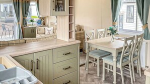 Una kitchenette con un lavabo, una mesa de comedor con sillas y una ventana con cortinas.