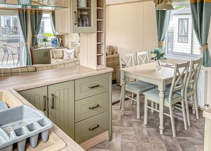 A kitchenette with a sink, a dining table with chairs, and a window with curtains.