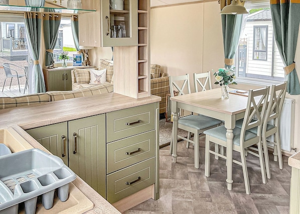Una kitchenette con un lavabo, una mesa de comedor con sillas y una ventana con cortinas.