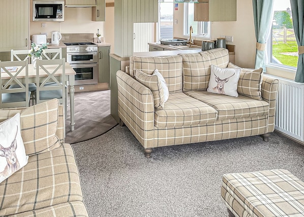 A cozy living area with a sofa set, a dining table with chairs, a kitchen with appliances, and a window with curtains. - Homely and stylish holiday home featuring your own private hot tub. (Laurenkirk)