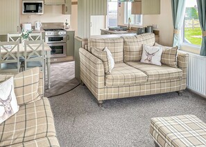 Una sala acogedora con sofá, una mesa de comedor con sillas, una cocina equipada y un ventanal con cortinas.