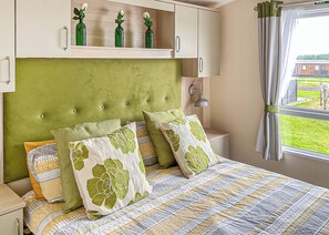 A bedroom with a green upholstered headboard, a patterned bedspread, and a window with a view of a building and greenery.