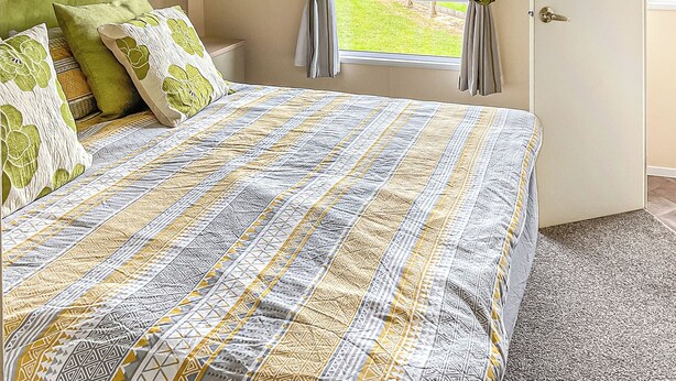 Un dormitorio con cama, cabecera verde, ventana con cortinas y vistas a un jardín.