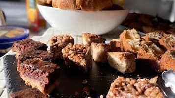 Variedad de productos horneados sobre una tabla de pizarra, incluyendo un bol de cruasanes y varios tipos de pan y pastelería.