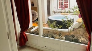 A room with a large window overlooking a small outdoor area with a hot tub and plants. - GA7COLORES (San Bartolome)