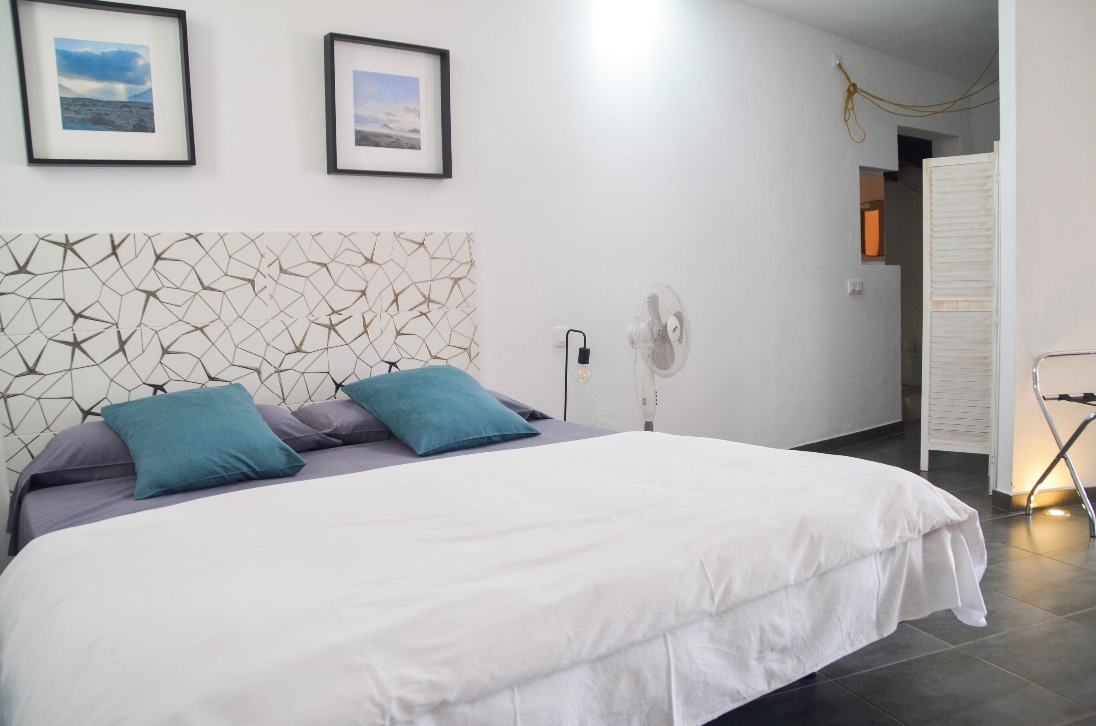 Una cama bien tendida con edredón blanco y gris, dos almohadas color turquesa y un cabecero con estampado geométrico.