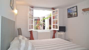 Un dormitorio con cama, ventana con cortinas, televisor sobre un mueble y un cuadro en la pared.