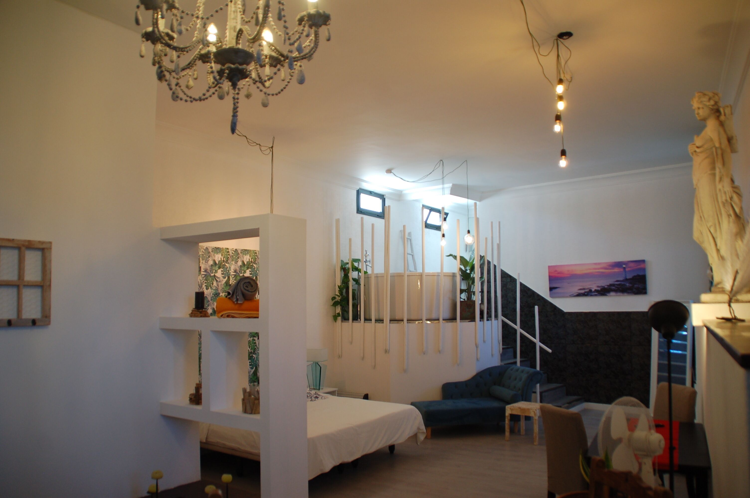 Una habitación con una cama, un sofá azul, una araña de cristal y una estatua.
