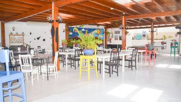 Un grand espace intérieur aménagé avec de nombreuses tables et chaises, des poutres en bois au plafond et diverses plantes en pot.