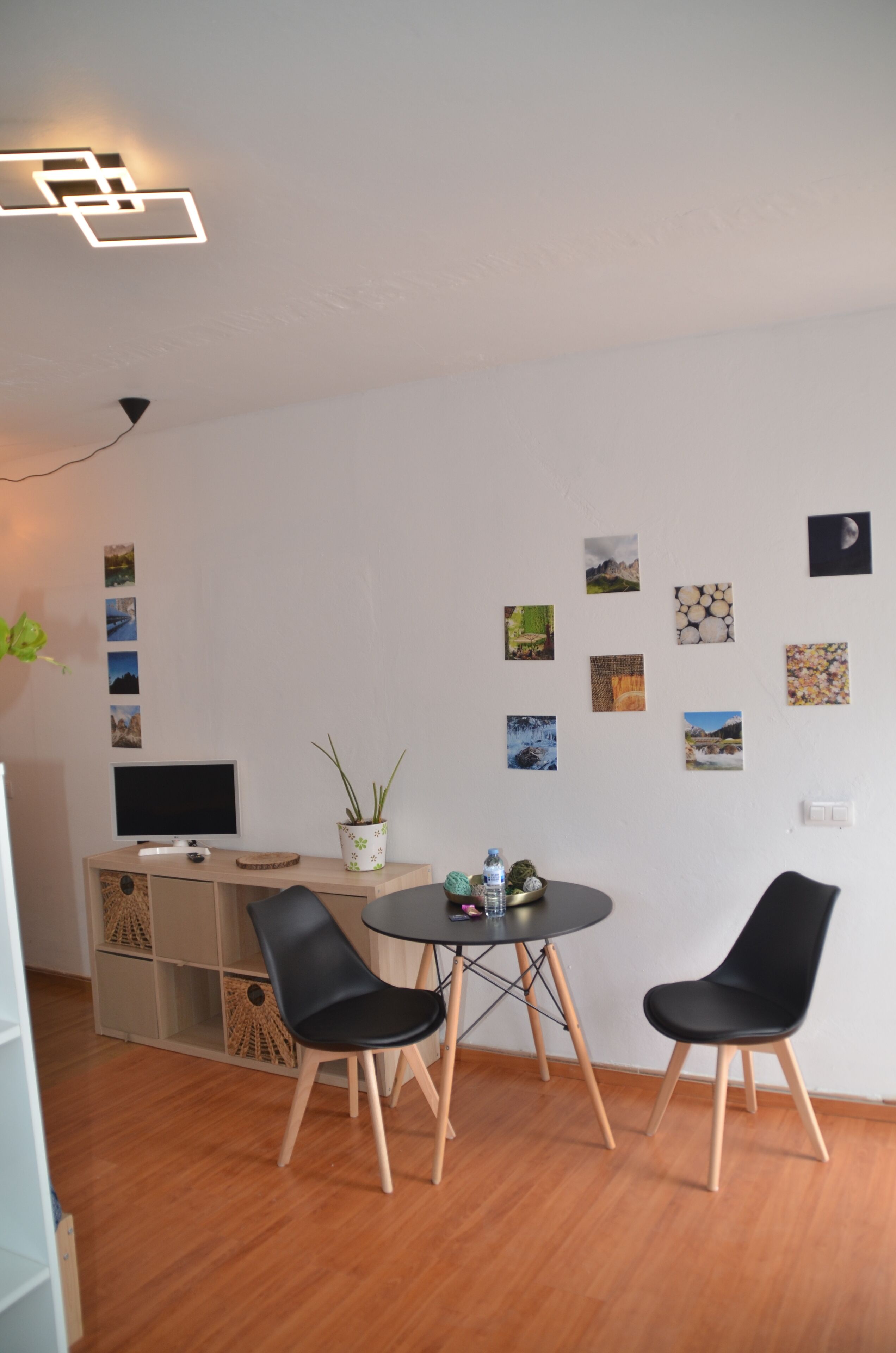 Ein modernes Wohnzimmer mit Flachbildfernseher, zwei schwarzen Sesseln, einem kleinen runden Tisch und einem Blumentopf.