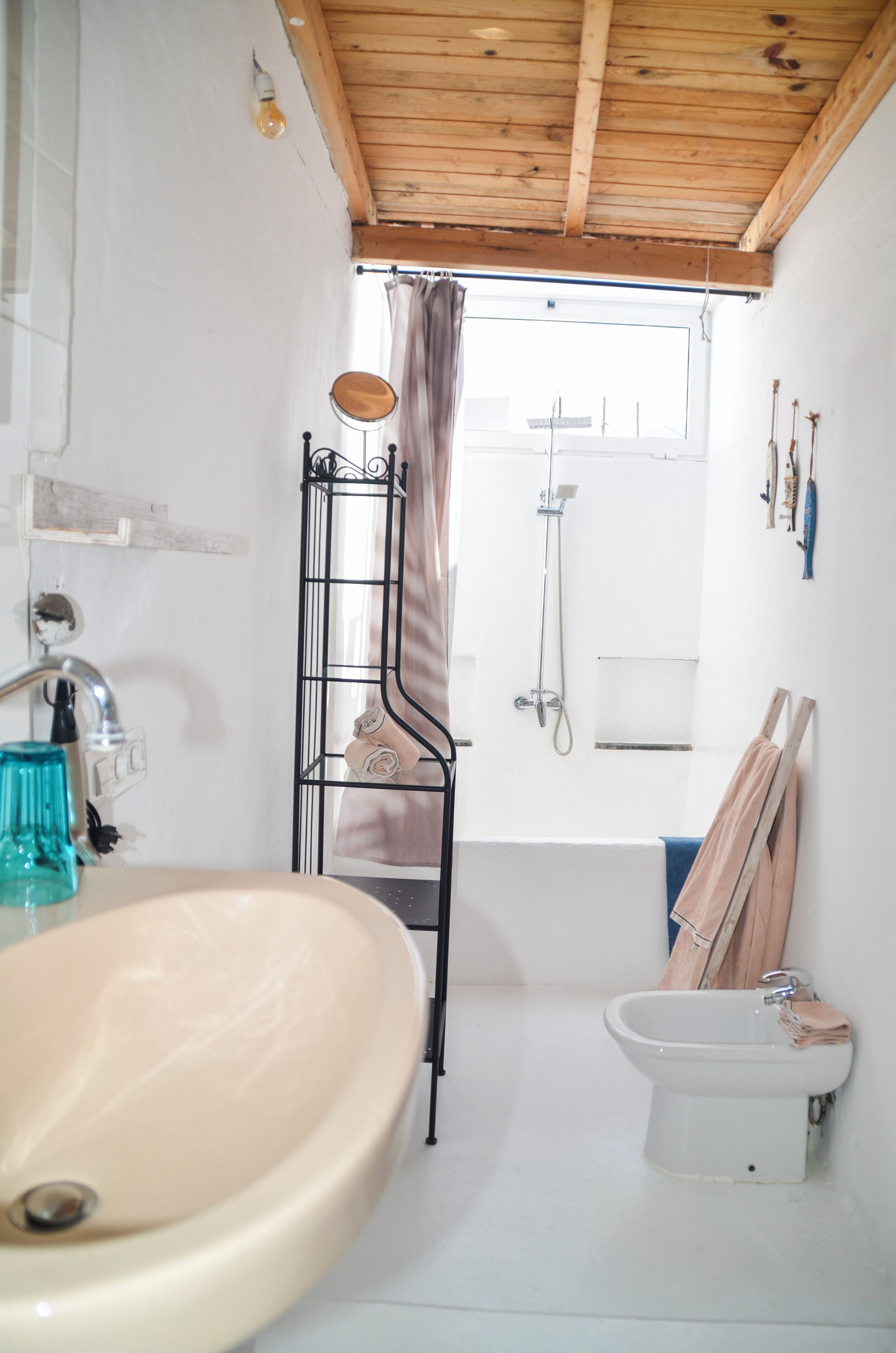 A bathroom with a wooden ceiling, a sink, a bidet, and a shower.